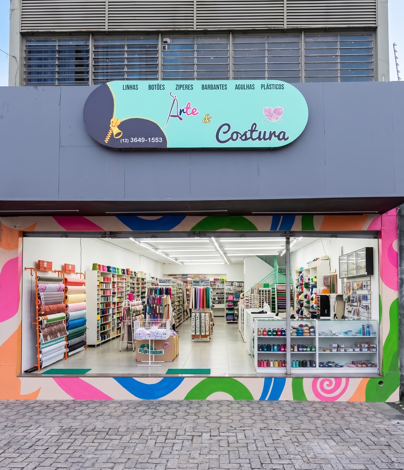 Fachada da loja Arte & Costura com placa colorida da marca, mural lateral e entrada com tecidos
